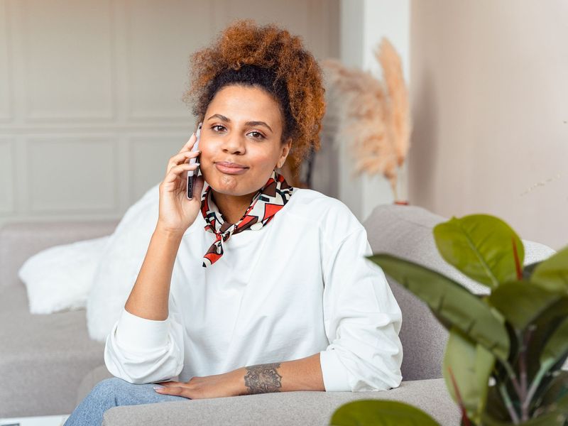 A Black woman on her couch, talking on the phone.